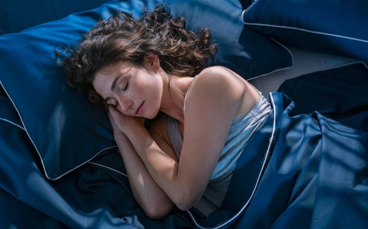 Femme couchée, les yeux fermés, dans un lit avec une parure de lit bleu nuit style satin.