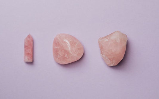Trois pierres de Quartz Rose, une brute à droite, une roulée au centre et une taillée en tour à gauche.  