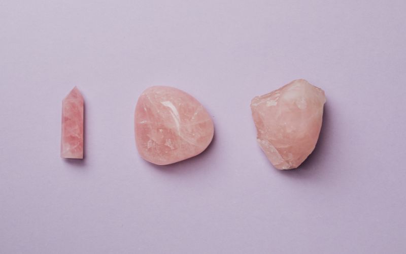 Trois pierres de Quartz Rose, une brute à droite, une roulée au centre et une taillée en tour à gauche.  