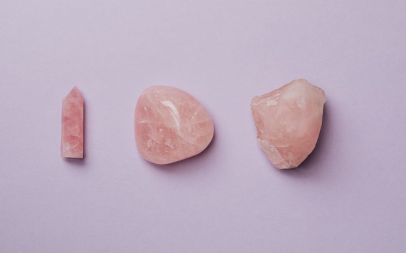 Trois pierres de Quartz Rose, une brute à droite, une roulée au centre et une taillée en tour à gauche.   Image