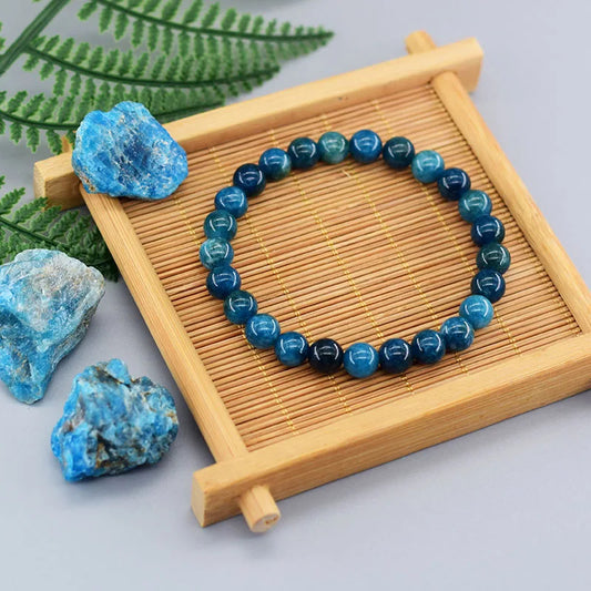 Bracelet en perles d'apatite bleue sur un support en bois avec des pierres à gauche et des feuilles