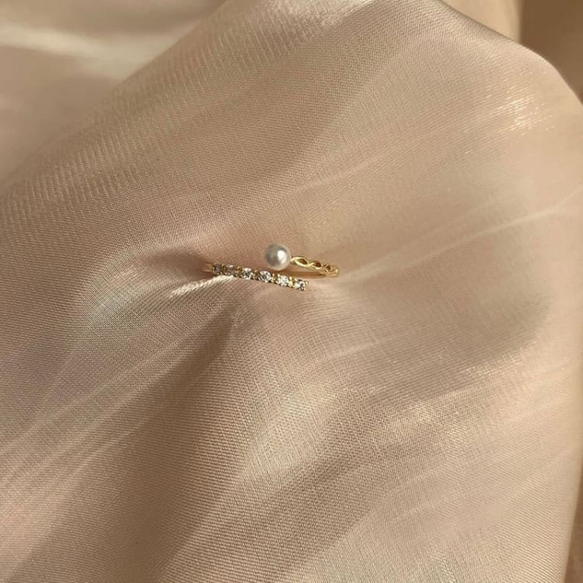 Bague ouverte dorée avec perle blanche et rangée de petites pierres sur tissu