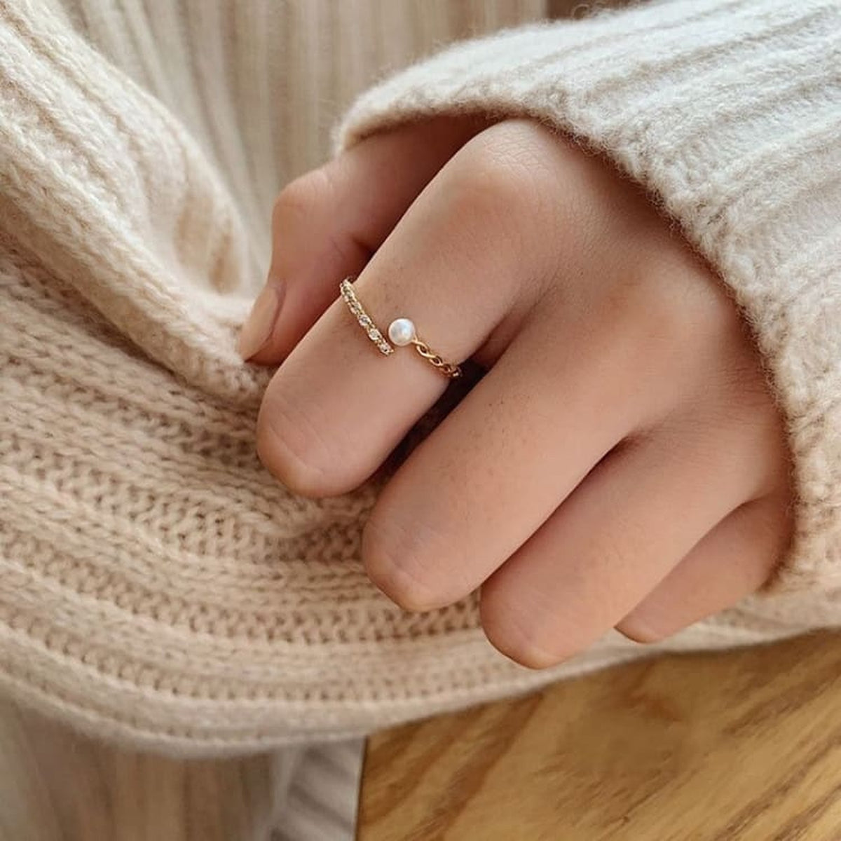 Bague fine dorée avec perle blanche portée avec une manche verte