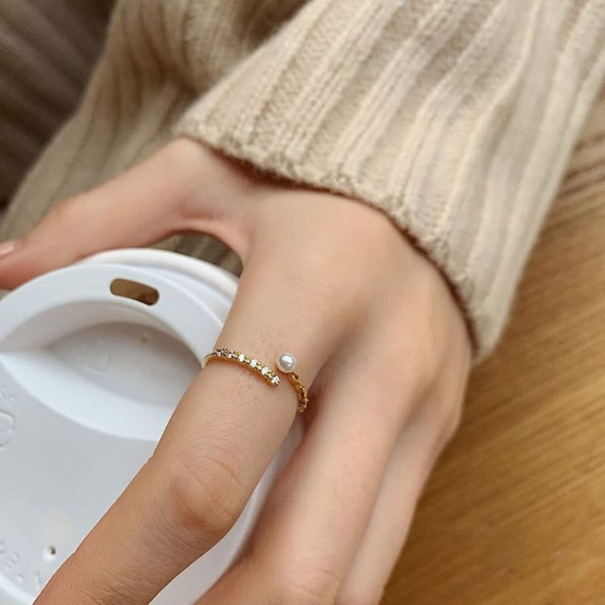 Bague dorée ajustable avec perle blanche portée sur une main