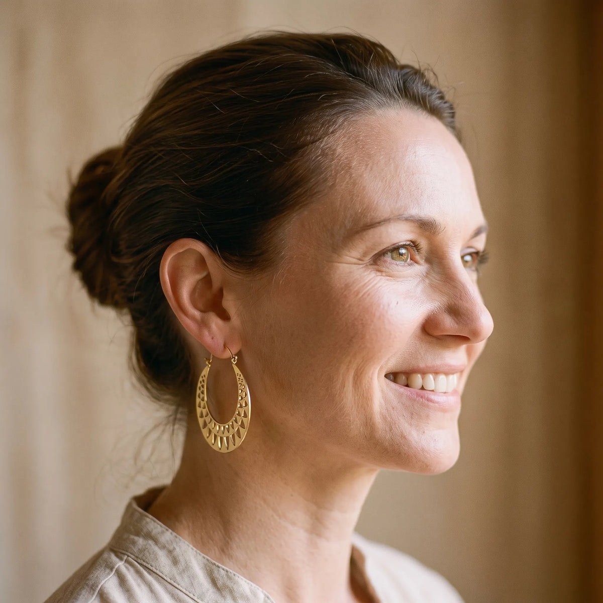 Boucles d'oreilles égyptiennes soleil doré portées par une femme souriante, oreille visible