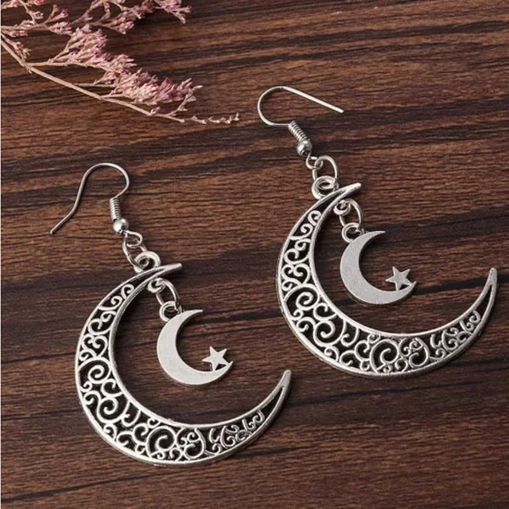 Boucles d'oreilles croissant de lune en métal argenté posées sur fond bois