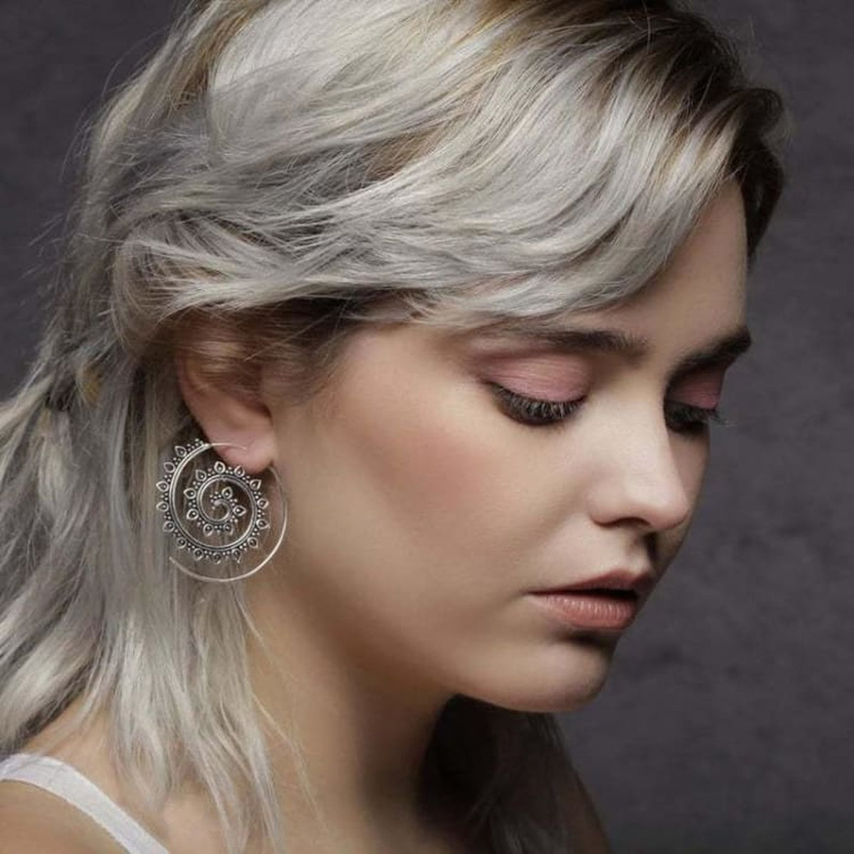 Boucles d'oreilles spirale portées par une femme, ambiance sombre