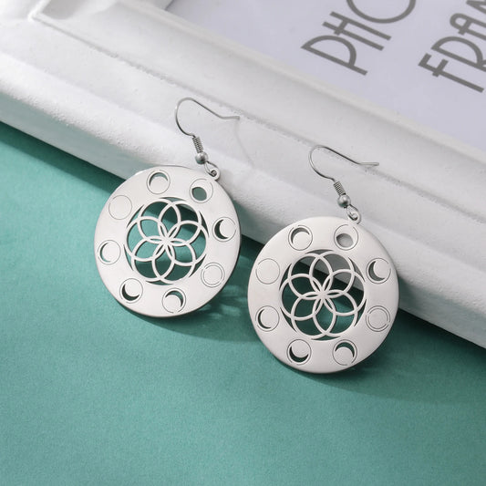 Boucles d'oreilles rondes avec mandalas en acier inoxydable posées sur un livre blanc sur fond vert