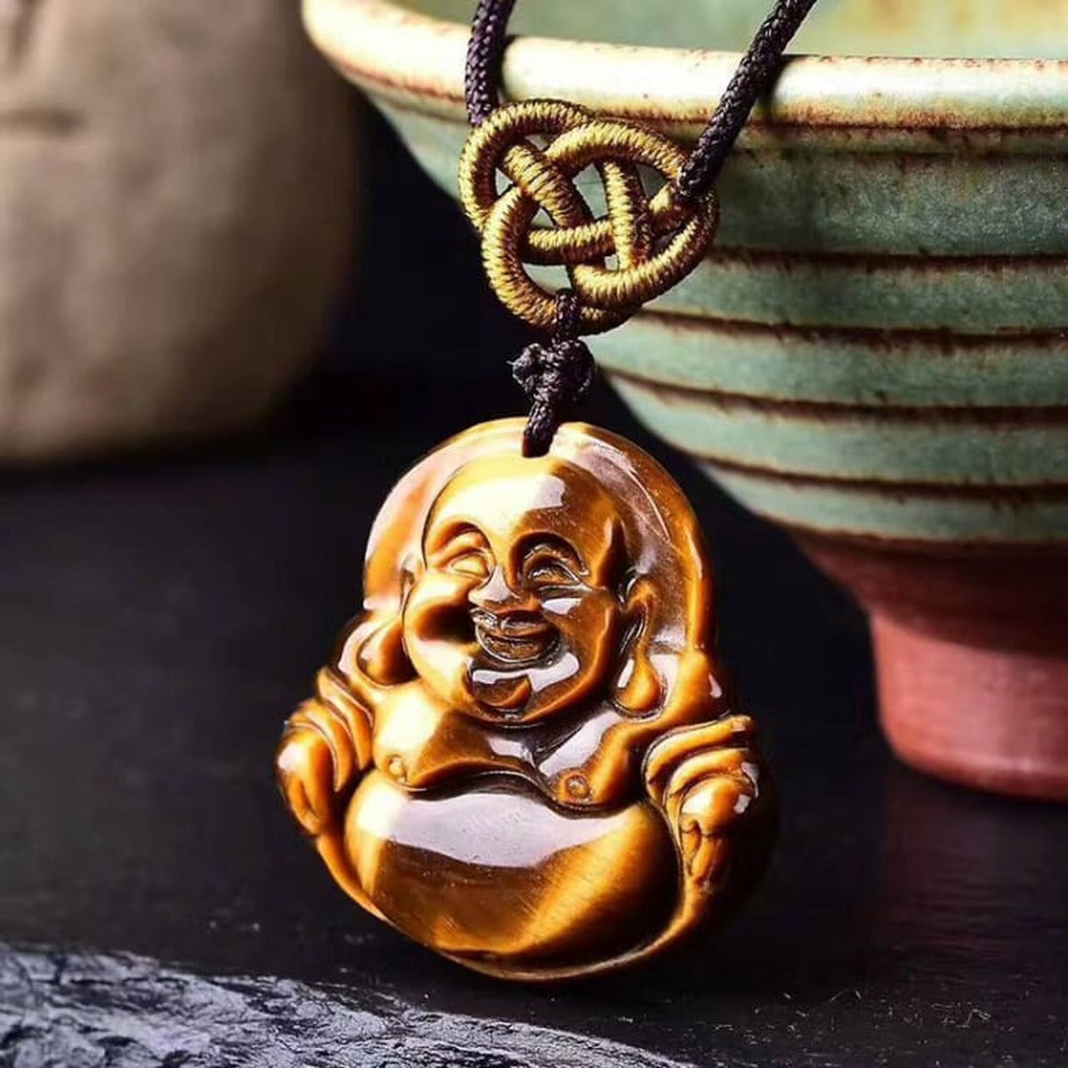 Collier Bouddha œil de tigre posé sur un décor zen avec galets et plante verte