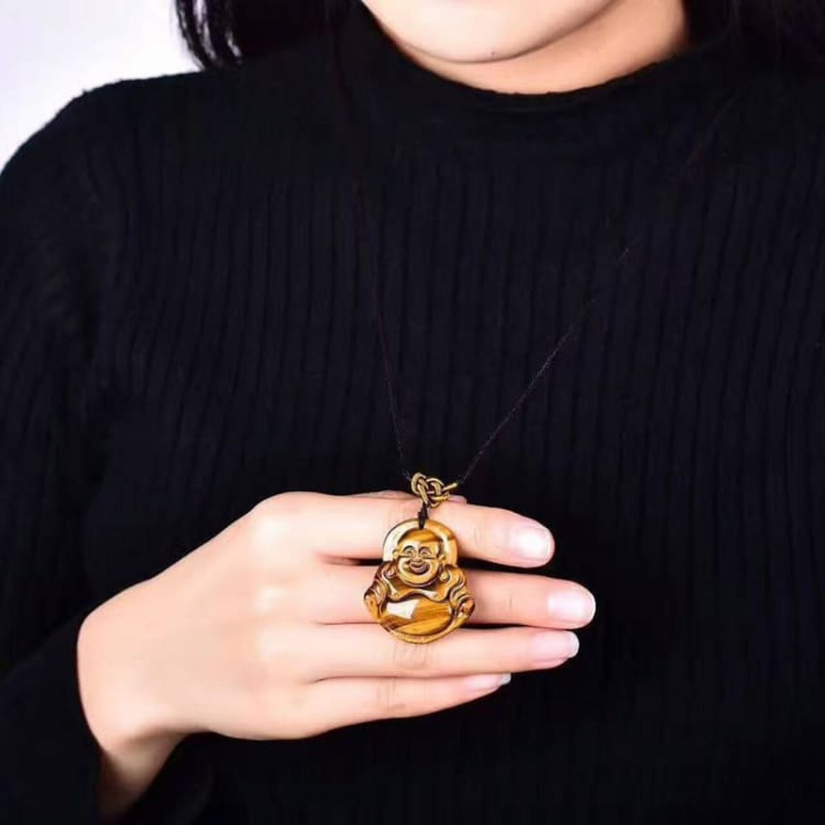 Collier pendentif Bouddha en œil de tigre porté, tenu délicatement dans la main
