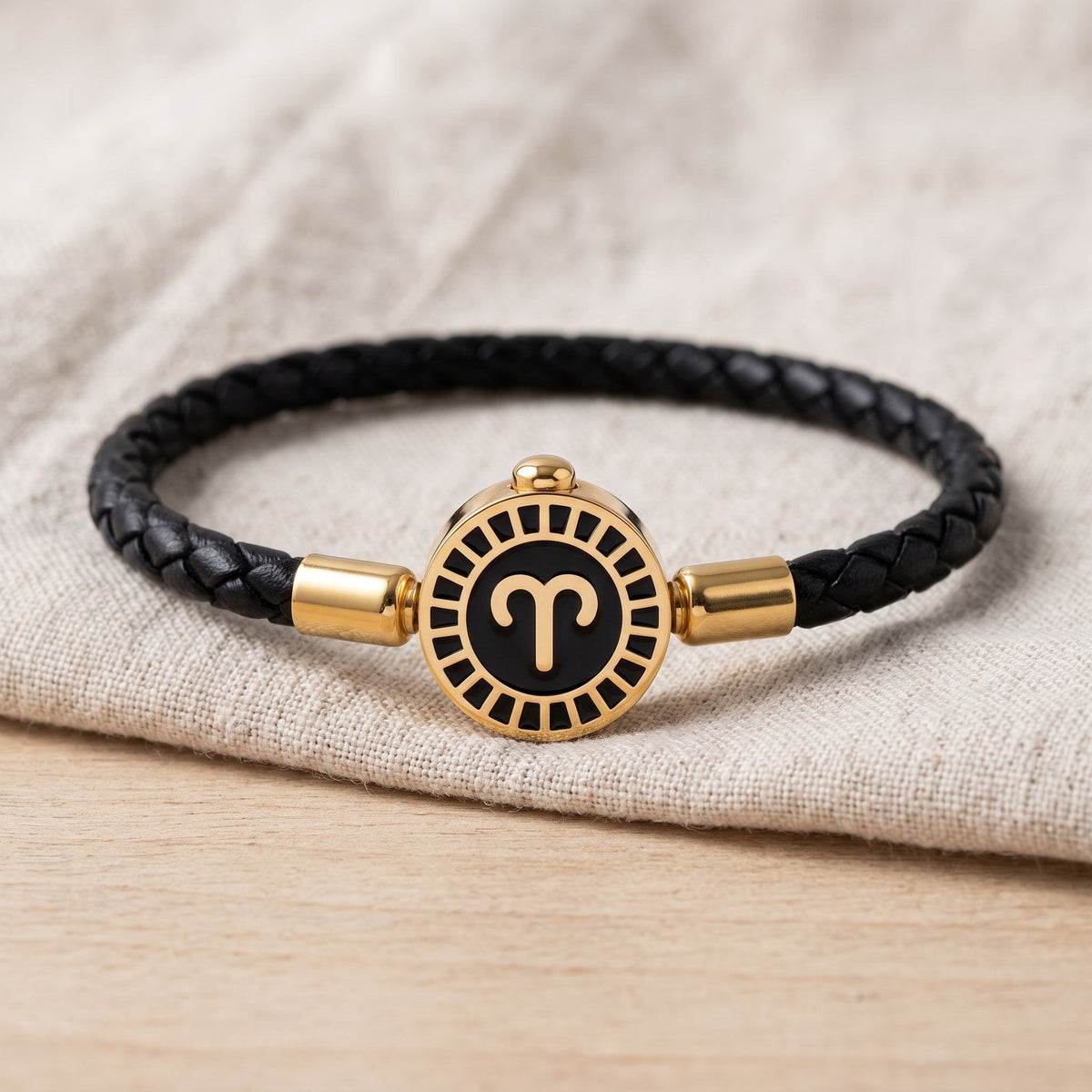 Bracelet signe astrologique Bélier, cordon tressé noir et médaillon rond doré, posé sur du lin écru