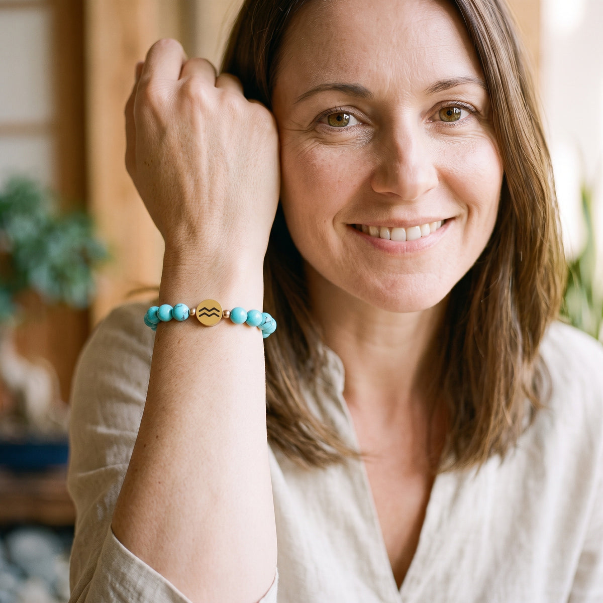 Femme souriante portant le bracelet signe astrologique en perles de turquoise avec son médaillon doré au poignet