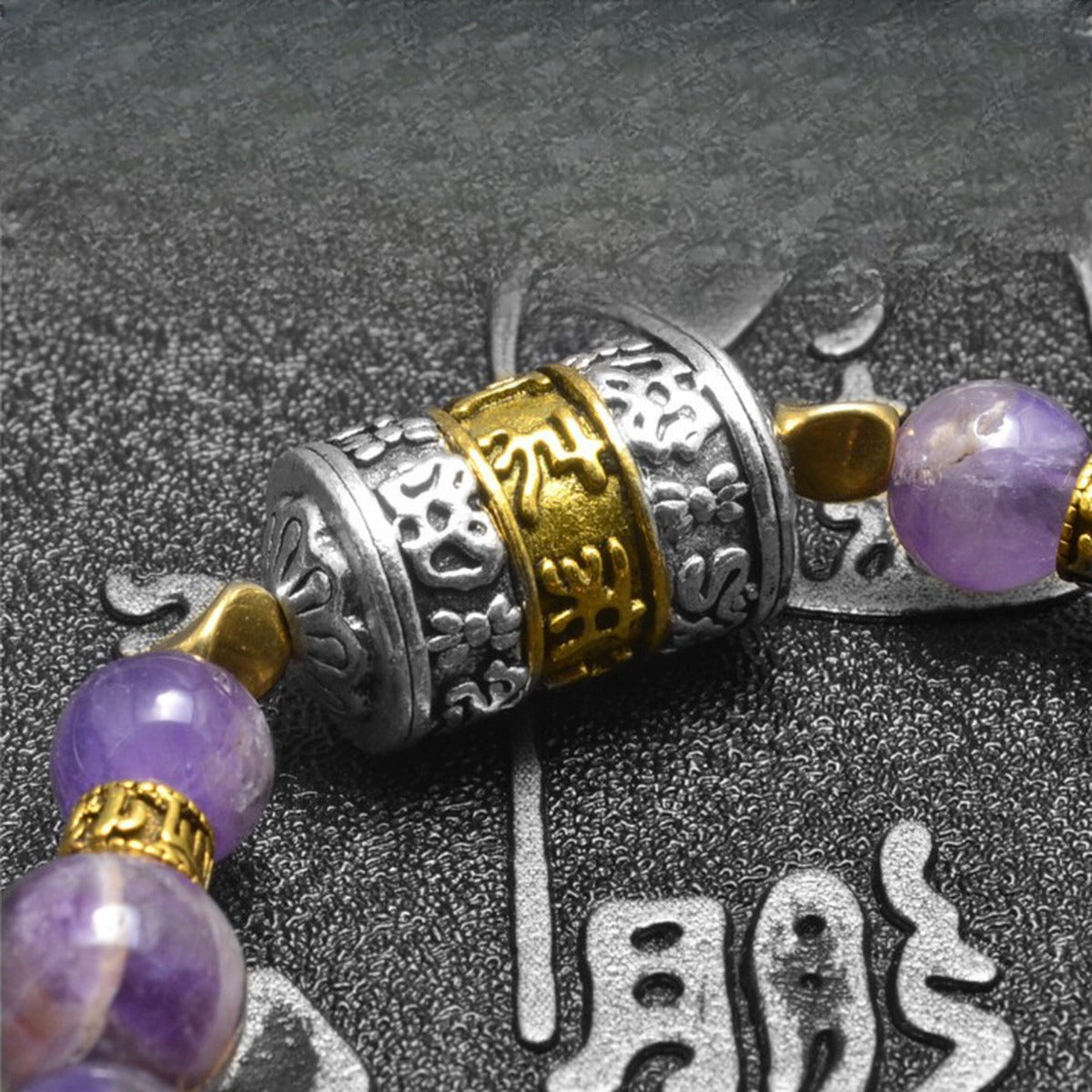Détail du cylindre central gravé du mantra Om Mani Padme Hum, entre perles d'améthyste violettes