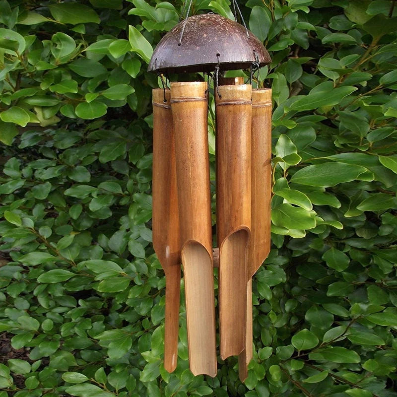 Carillon en bambou naturel avec coquille de coco devant un buisson vert