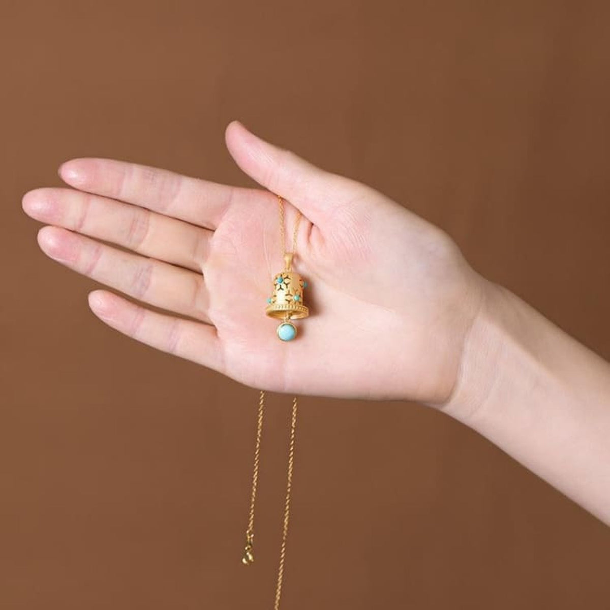 Collier cloche dorée présenté dans la main pour montrer son échelle