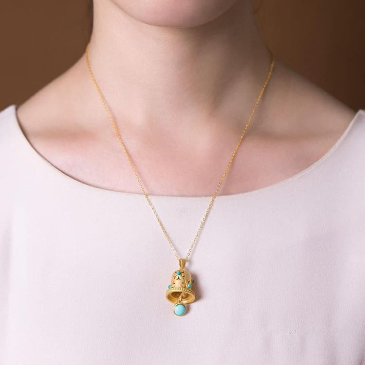 Collier cloche dorée porté au cou avec chaîne fine