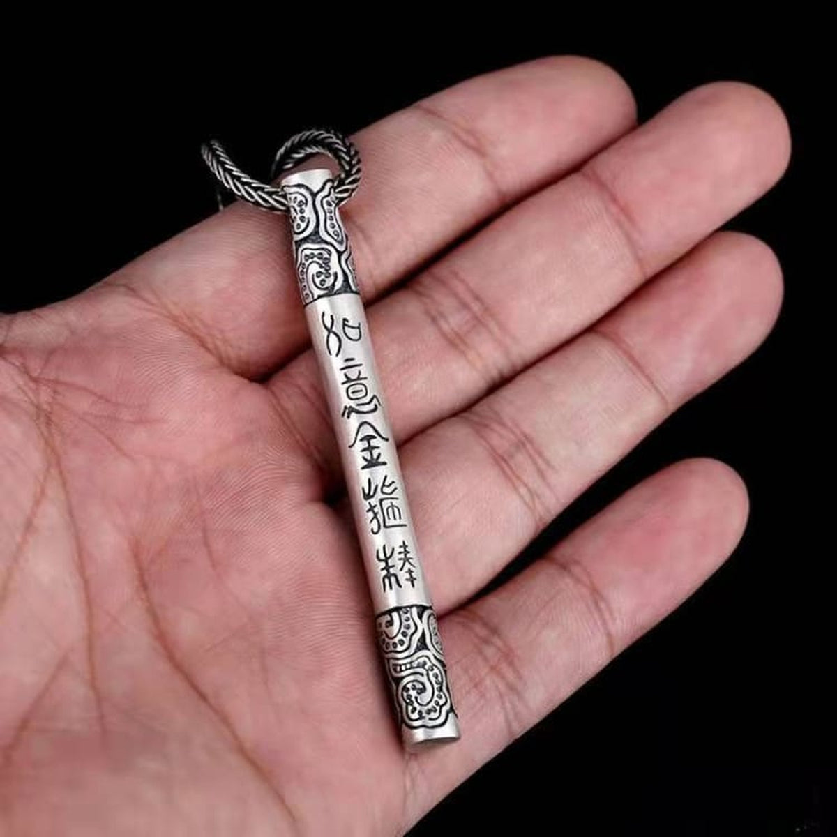Détail du pendentif bâton argenté tenu entre les doigts