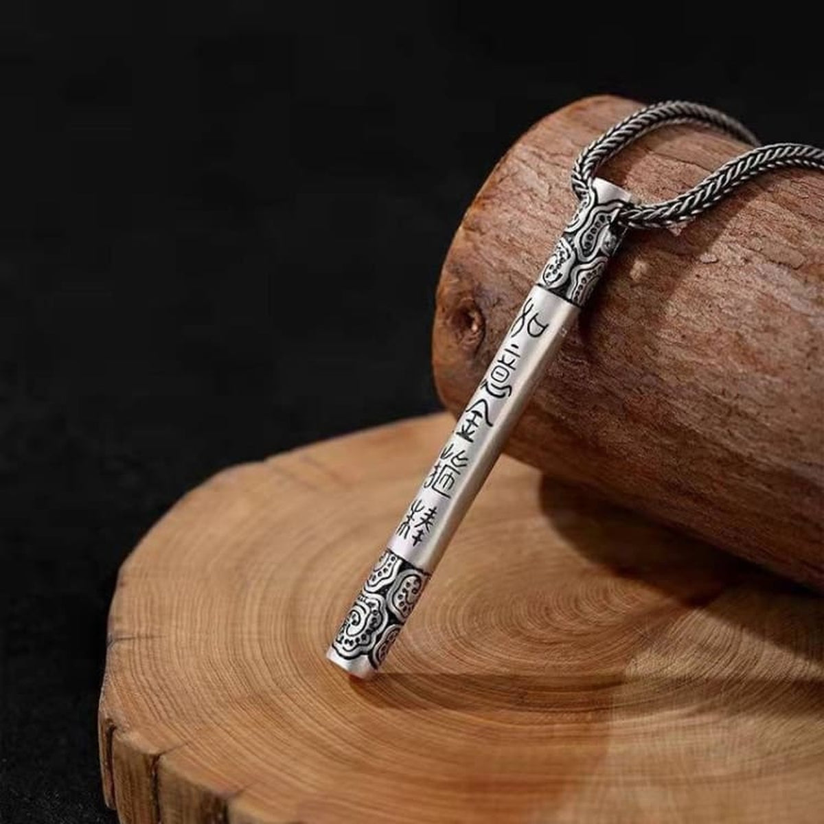 Pendentif bâton argenté du collier Wukong posé sur du bois
