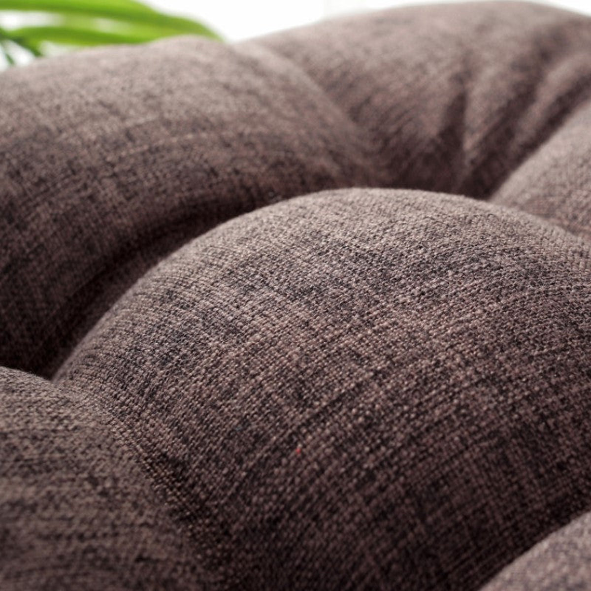 Gros plan sur la texture chinée et le capitonnage du coussin de méditation marron, plante verte en arrière-plan flou