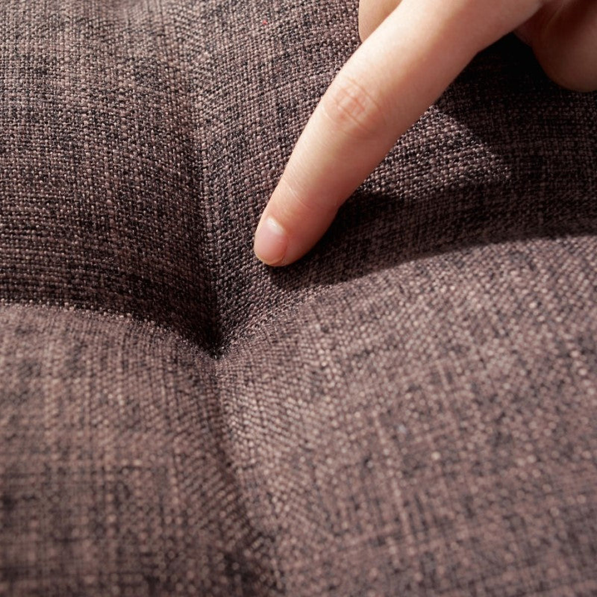 Détail de la densité du coussin de méditation, un doigt enfoncé dans le tissu capitonné marron