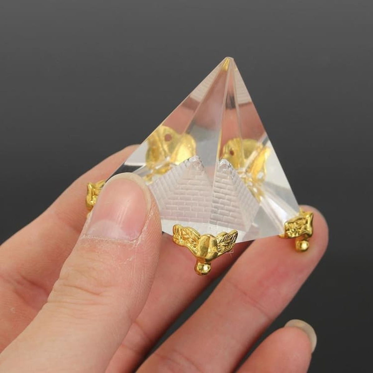 Petite pyramide transparente aux détails dorés tenue entre les doigts