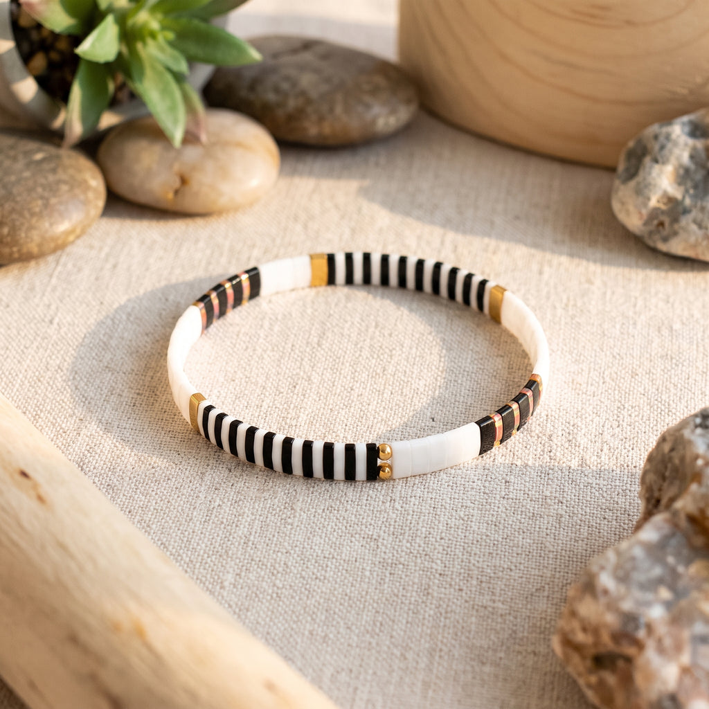 Bracelet en perles de verre japonaises posé sur lin beige, galets et plante verte