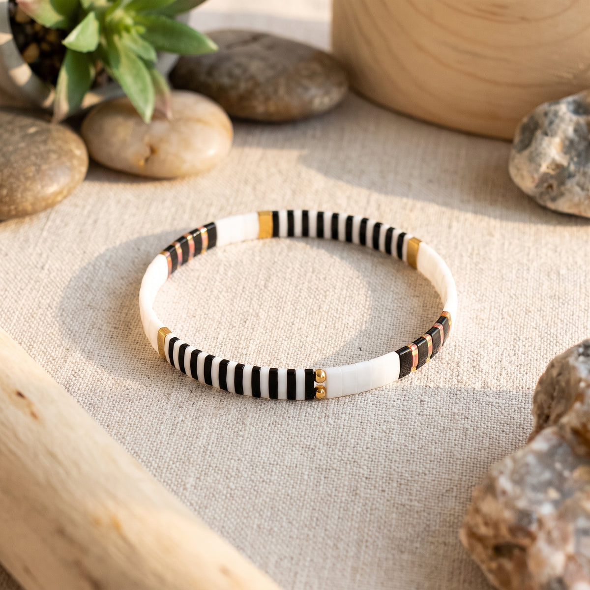 Bracelet en perles de verre japonaises posé sur lin beige, galets et plante verte