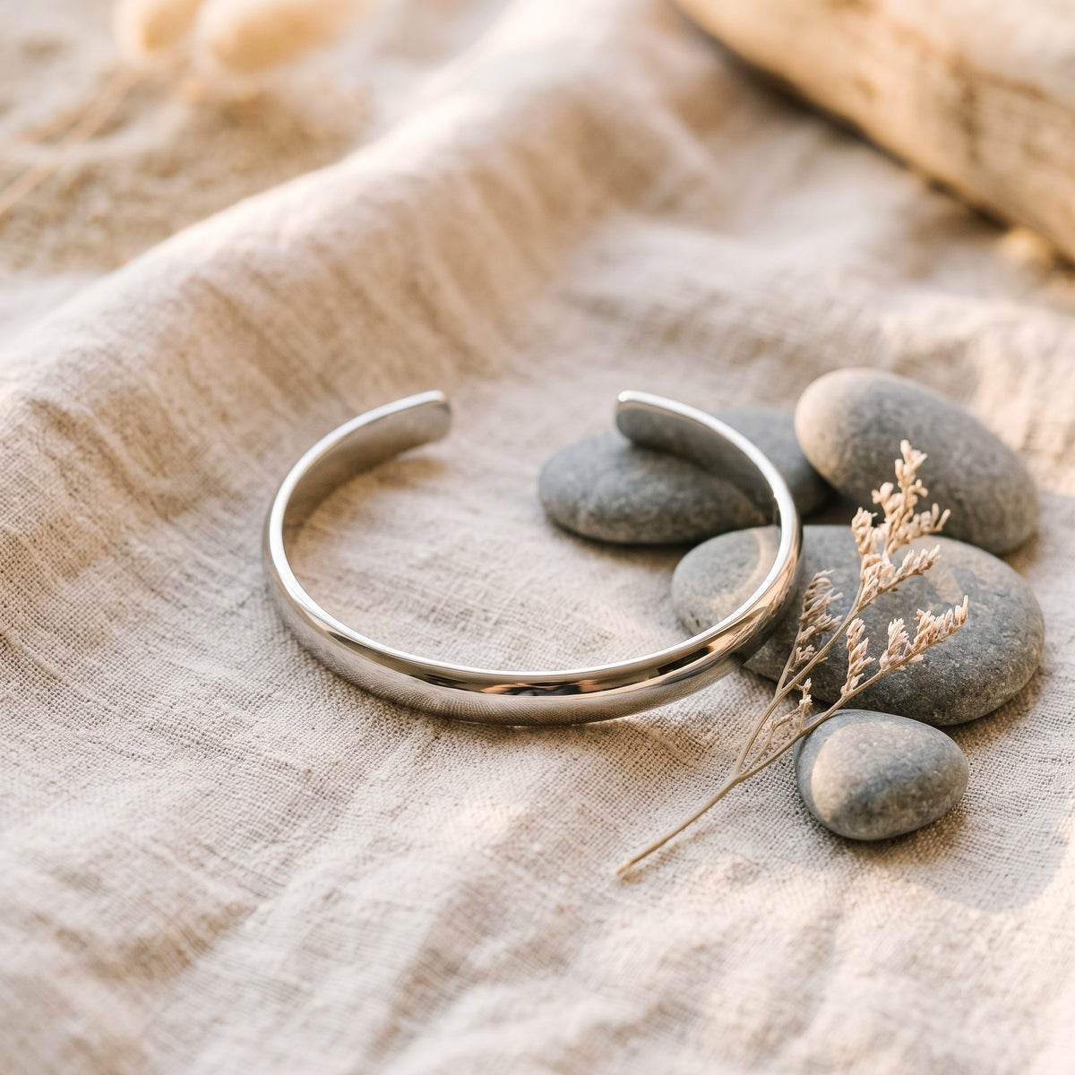 Bracelet jonc argenté posé sur lin froissé avec galets et végétal - ambiance zen Le Temple Yogi