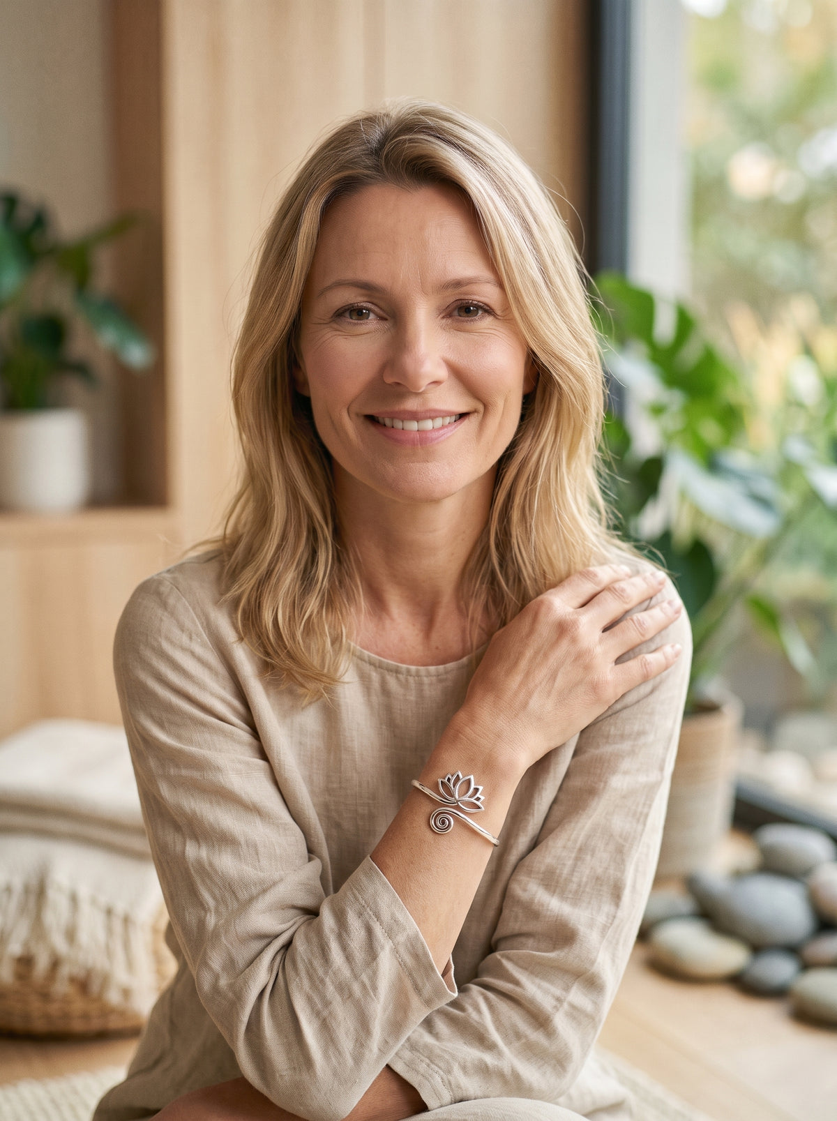 Femme souriante portant un bracelet jonc Fleur de Lotus argente au poignet, modele bien-etre en interieur zen