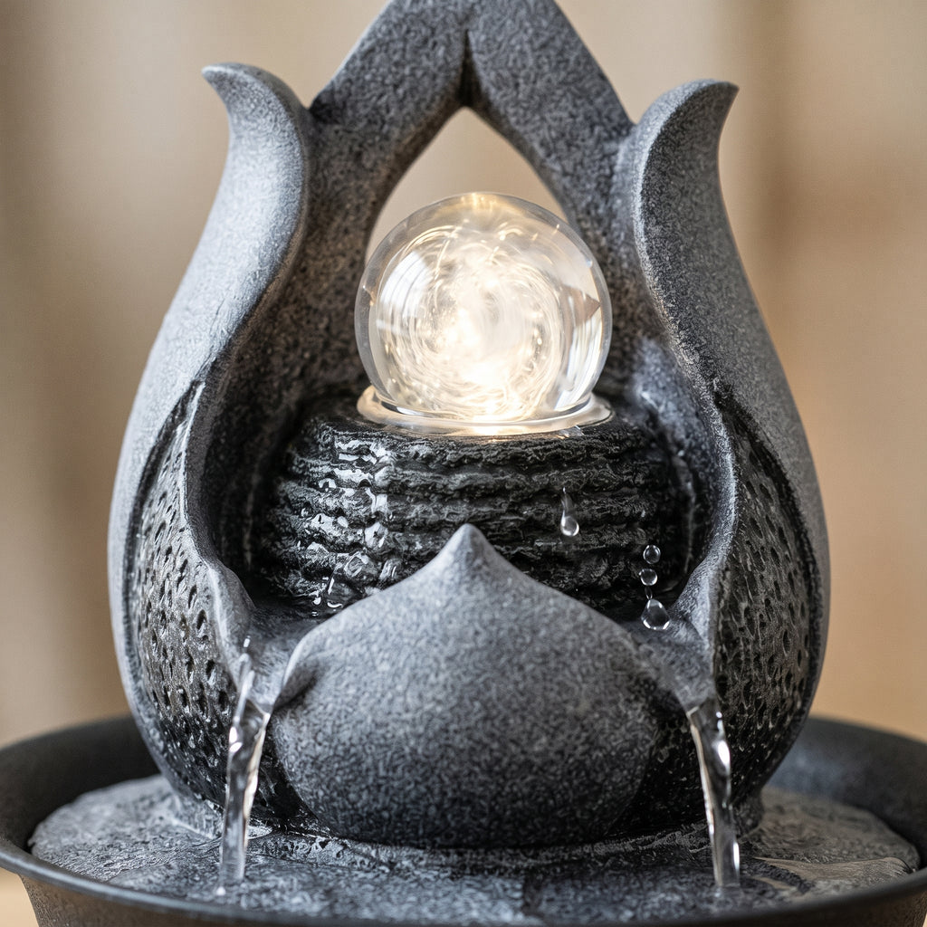 Gros plan sur la boule lumineuse et les filets d'eau de la fontaine décorative grise
