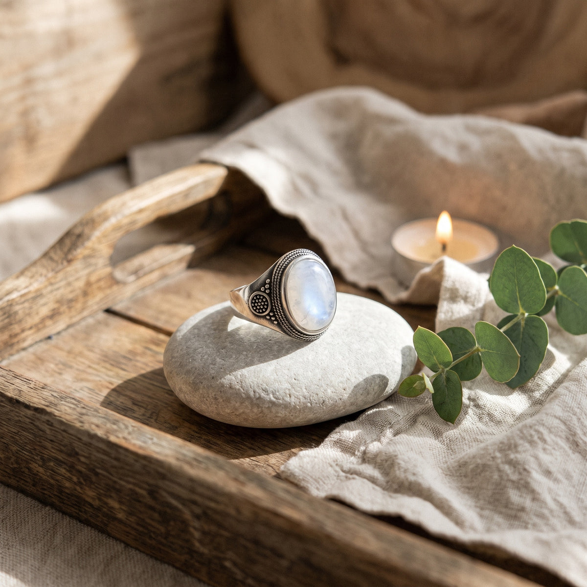 Bague chevalière pierre de lune posée sur un galet, ambiance zen lin et bois clair