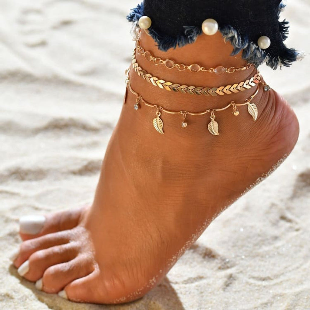 Bracelet de cheville boheme triple rang dore porte a la cheville sur sable, jean en denim perle