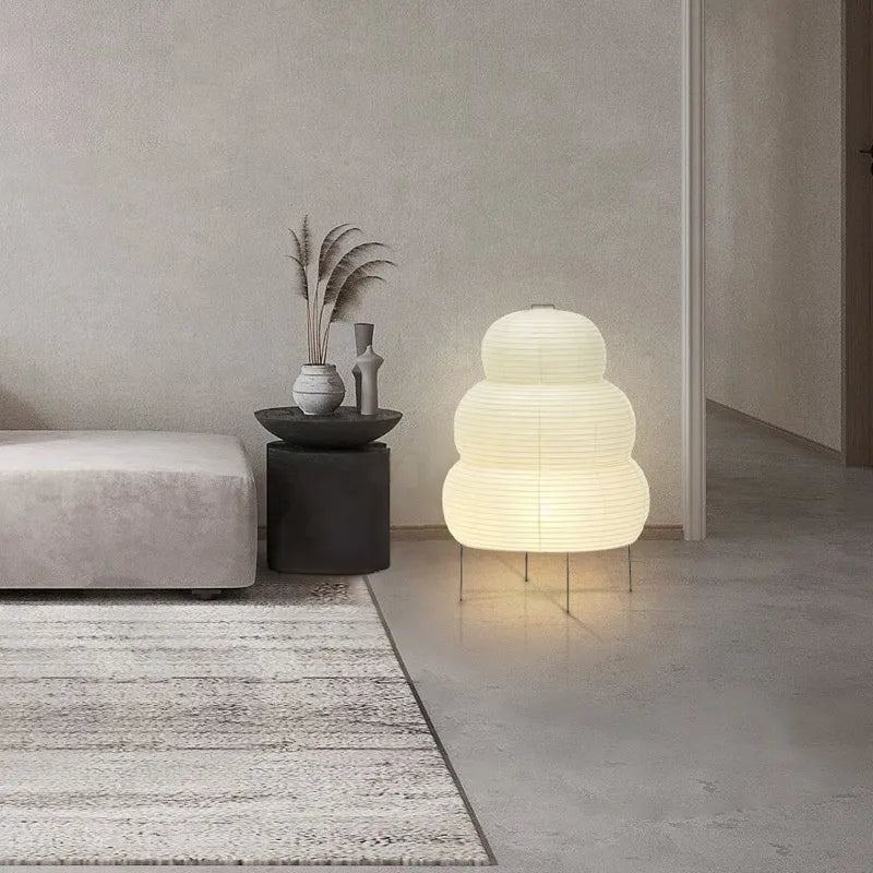 Lampe zen de style japonais en papier et métal dans une pièce sur fond gris avec un canapé et une table avec une plante à gauche