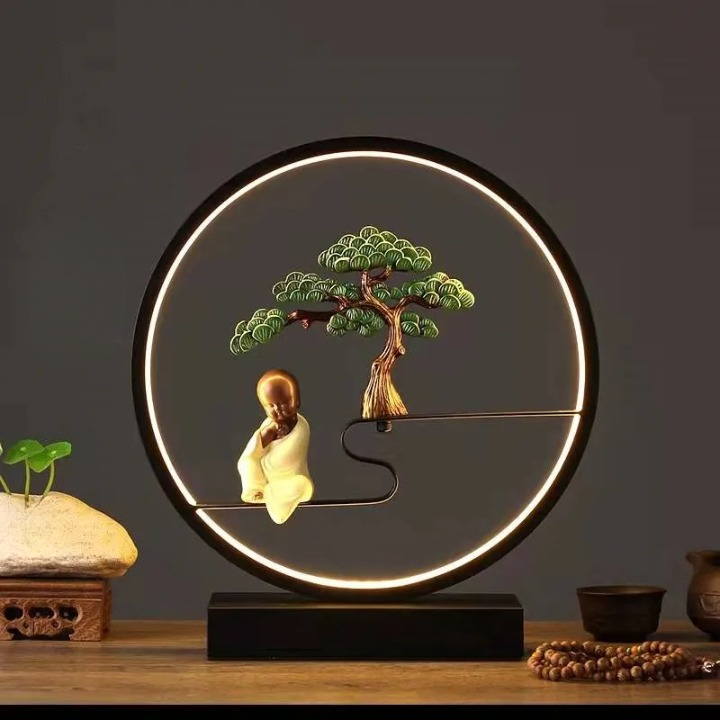 Lampe zen ronde avec bouddha et un arbre en aluminium sur un meuble avec des objets sur fond gris