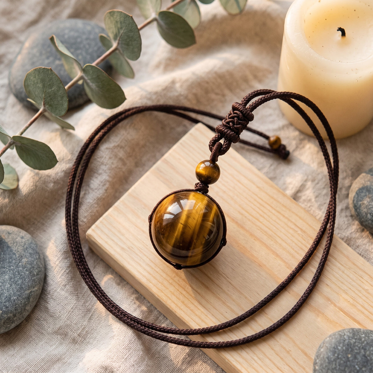 Collier en oeil de tigre posé sur du lin et du bois clair, sphère polie et cordon tressé
