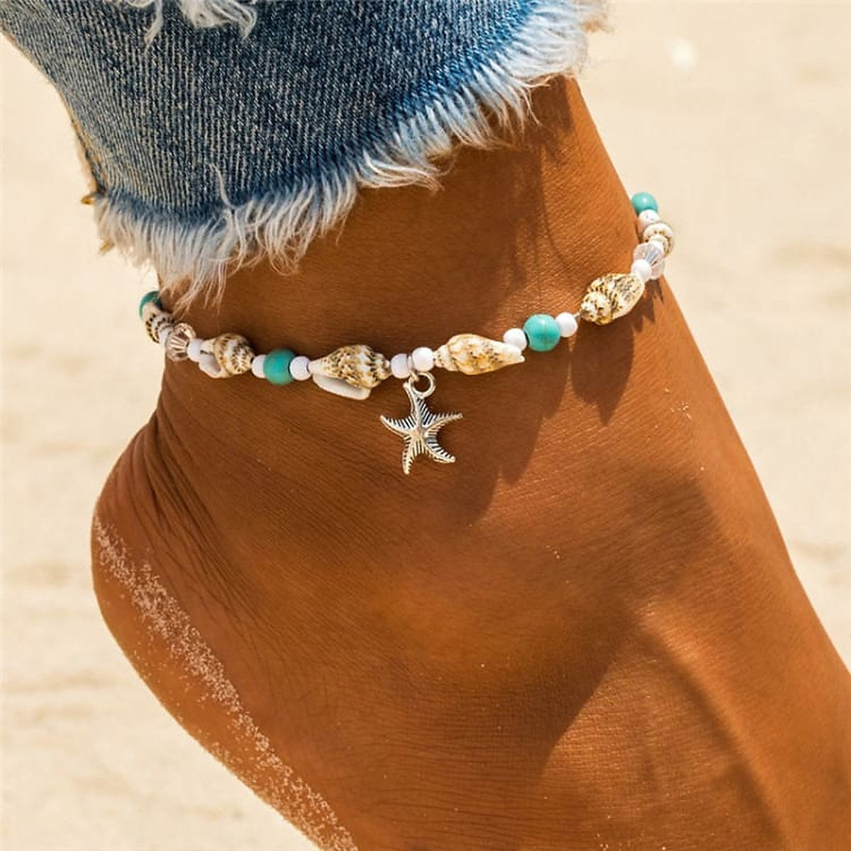 Bracelet de cheville femme en coquillages porté sur une cheville, plage de sable