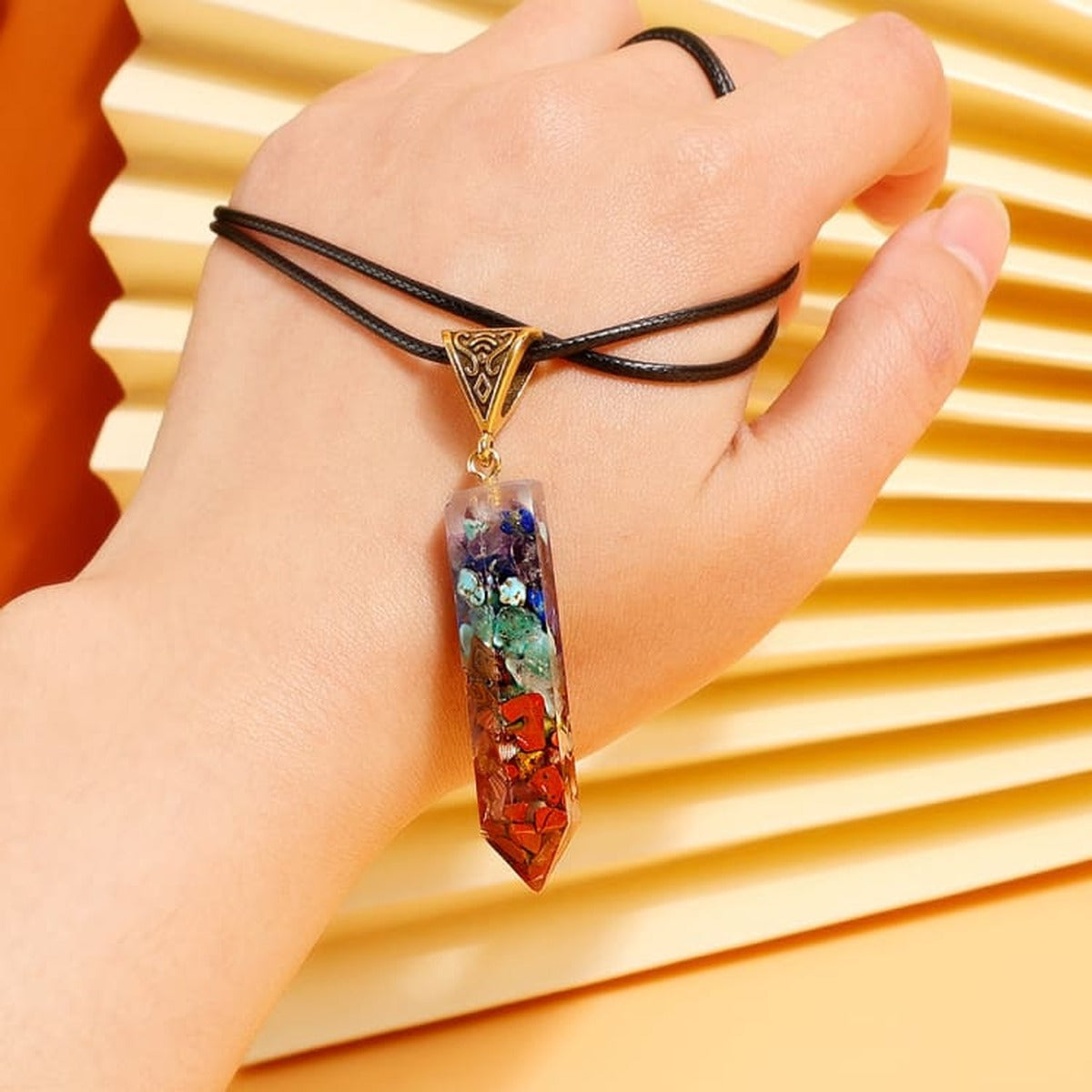 Collier pendentif 7 chakras tenu dans la main, cordon enroulé