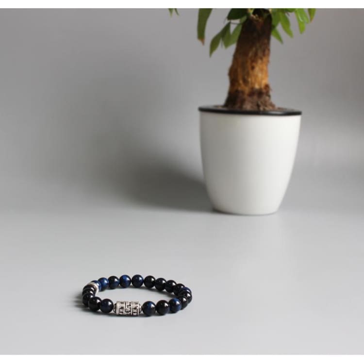 Bracelet Om posé à plat, la bande claire des perles visible sous la lumière