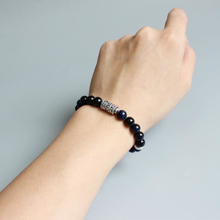 Bracelet Om porté au poignet, perles bleu nuit et ornement argenté